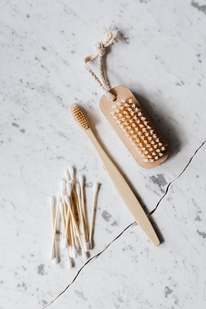 Top view composition of a wooden cleaning brush and cotton swab arranged on a marble surface beside a wooden toothbrush on line chop